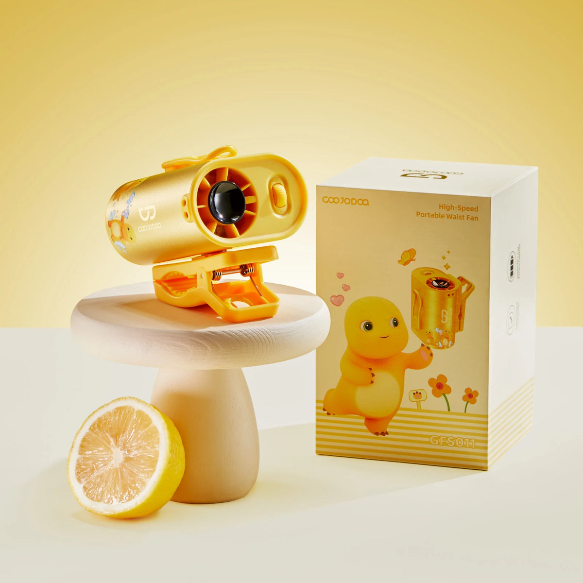 Yellow portable fan on a stand with a matching box and lemon on a light yellow background