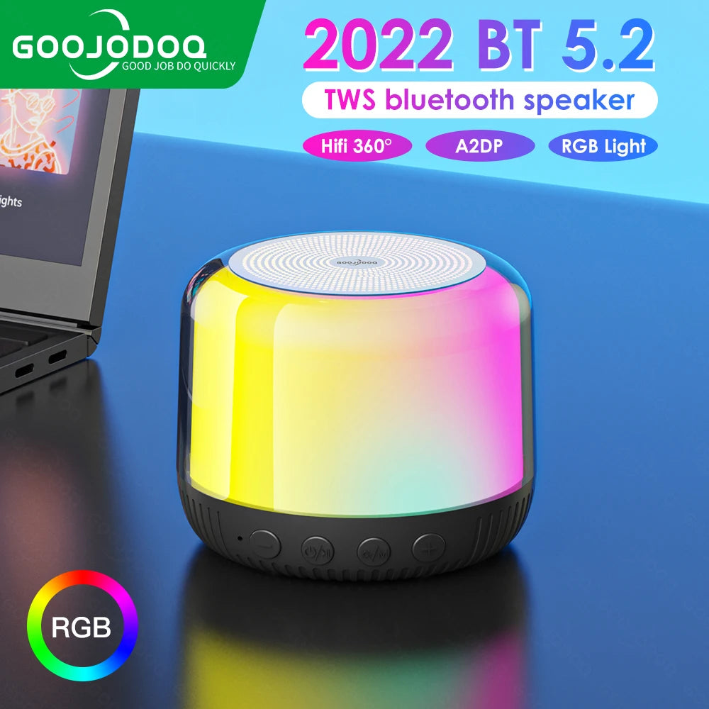 A small, cylindrical Bluetooth speaker with multicolored RGB lights at the top, placed on a flat surface with a laptop in the background.