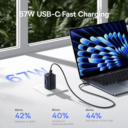 Laptop with 67W USB-C fast charging adapter on a white surface with greenery outside.