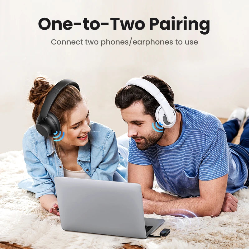 Two people using headphones with a laptop, lying on a bed.