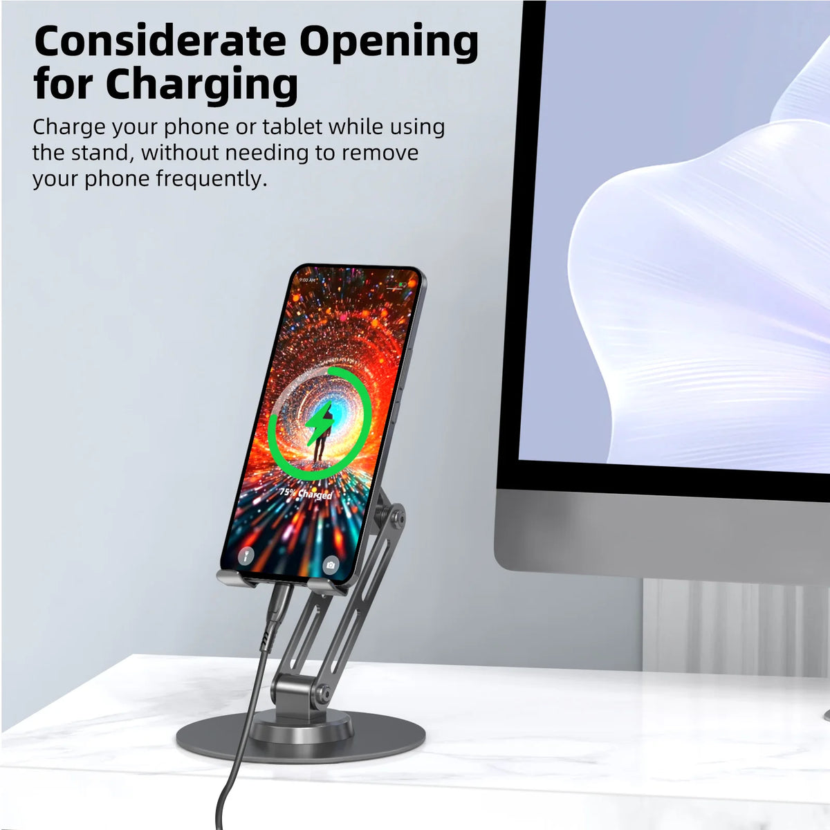 Phone stand with charging cable next to a computer monitor on a white surface.