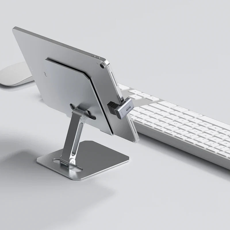 Metallic tablet stand holding a tablet next to a keyboard on a light gray surface